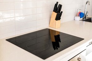 A kitchen with a black induction cooktop, a wooden knife block, and a stainless steel faucet. - Welles St | Christchurch CBD | Sleeps 4 | Balcony (Christchurch)