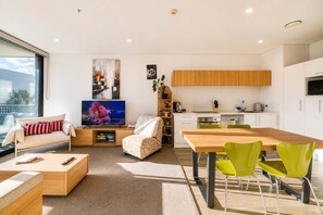 Ein modernes Wohnzimmer mit einer Couch, einem Fernseher, einem Essbereich mit Stühlen und einer Küche mit Schränken.