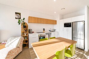 Eine moderne Küche mit weißen Schränken, einem Edelstahl-Kühlschrank und einem Essbereich mit einem Holztisch und grünen Stühlen.