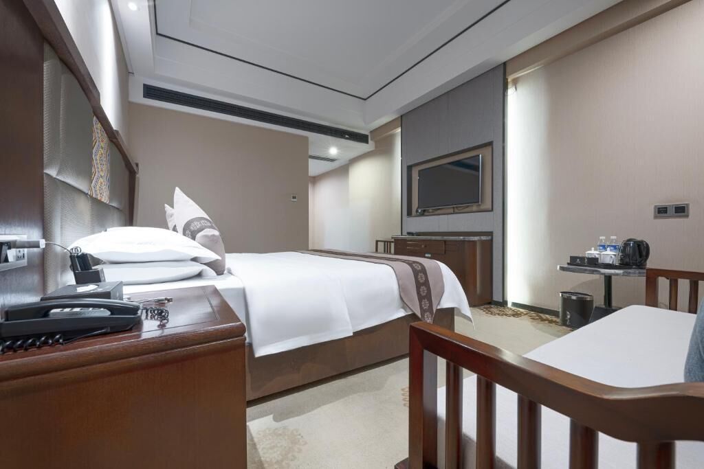 Habitación de hotel con cama, mesita de noche, escritorio, silla, televisión y una pequeña zona de kitchenette.