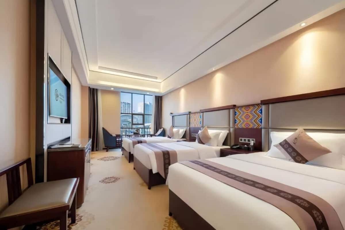 Habitación de hotel con tres camas, un escritorio, una silla y un televisor.