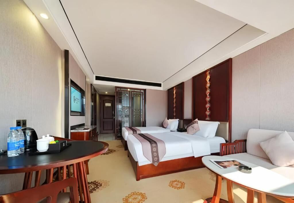 A hotel room with two beds, a dining table, a sofa, and a TV.