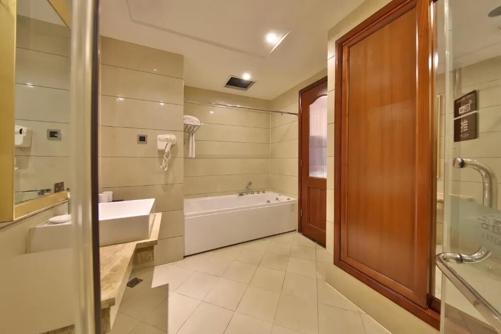 A modern bathroom with a bathtub, a vanity, a shower area, and a wooden door.