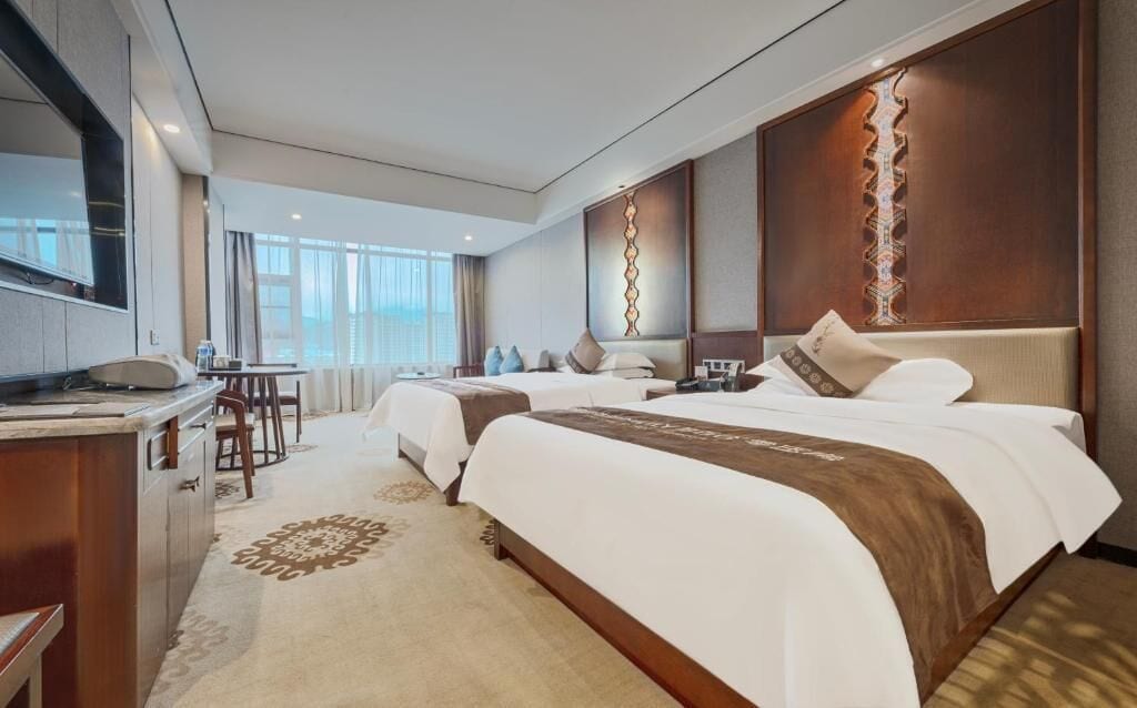 A hotel room with two beds, a desk, and a view of the city.