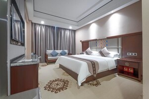 Ein Hotelzimmer mit Bett, Nachttischen, einem Spiegel, Vorhängen und einem gemusterten Teppich.