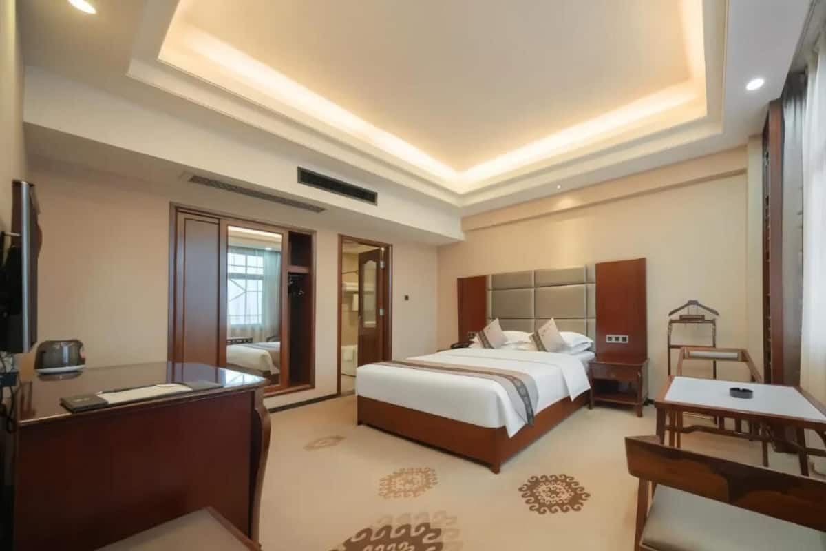 Una habitación de hotel con cama, mesita de noche, escritorio y espejo.