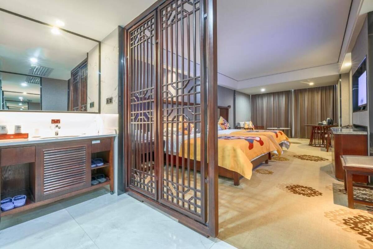 Habitación de hotel con una cama grande, un escritorio, un televisor, un baño con espejo y lavabo, y una separación decorativa.