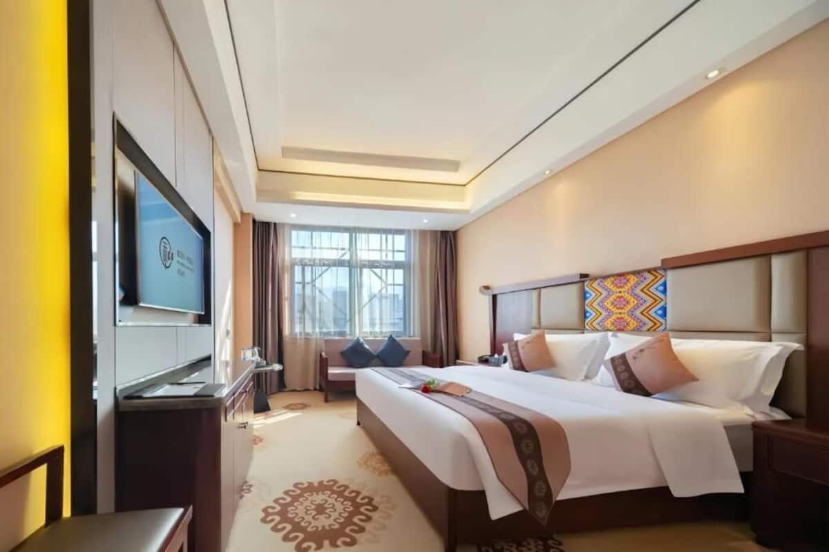 Una habitación de hotel con una cama grande, televisión, escritorio y ventana con cortinas.