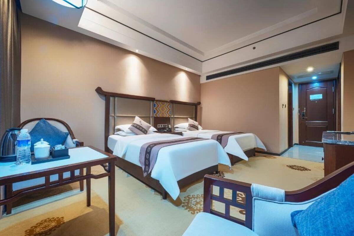 Habitación de hotel con dos camas, un escritorio, una silla y una mesita con una botella de agua y una taza.