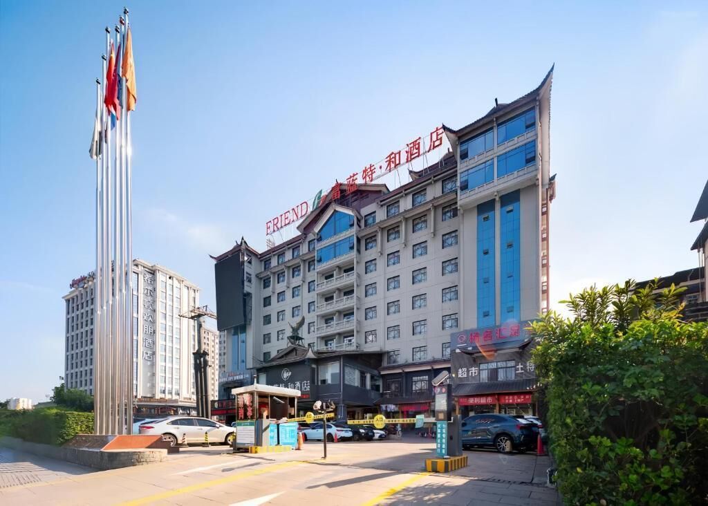 A multi-story hotel with a prominent sign, a tall flagpole with multiple flags, and a parking area with several cars.