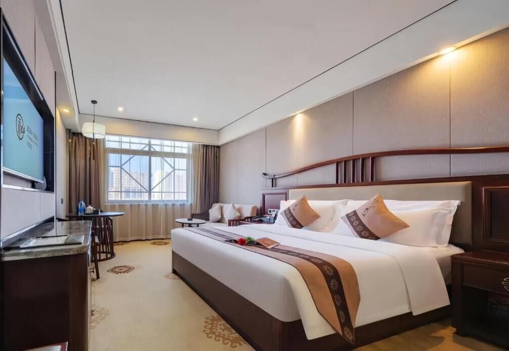 A hotel room with a large bed, a desk, a chair, a TV, and a window with curtains.