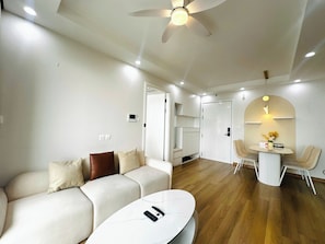 A modern living room with a sofa, a coffee table, a ceiling fan, and a dining area with chairs and a small table. - Tami Stay - Vinhomes D'Capitale (Cau Giay)