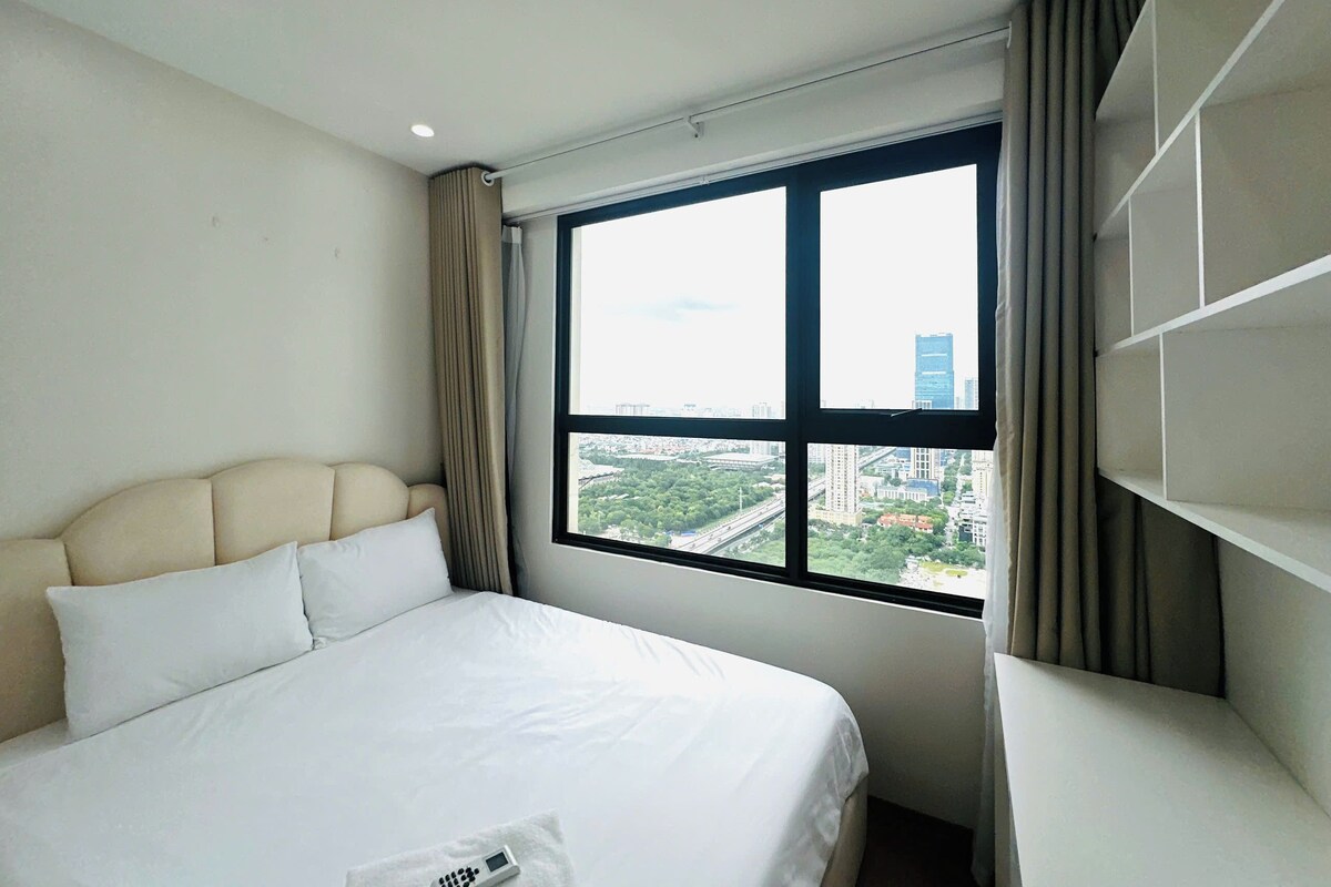 A hotel room with a bed, a window with a city view, and a built-in shelf.