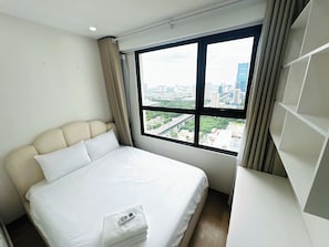 A hotel room with a large bed, a view of the city through a window, and a white wall. - Tami Stay - Vinhomes D'Capitale (Cau Giay)