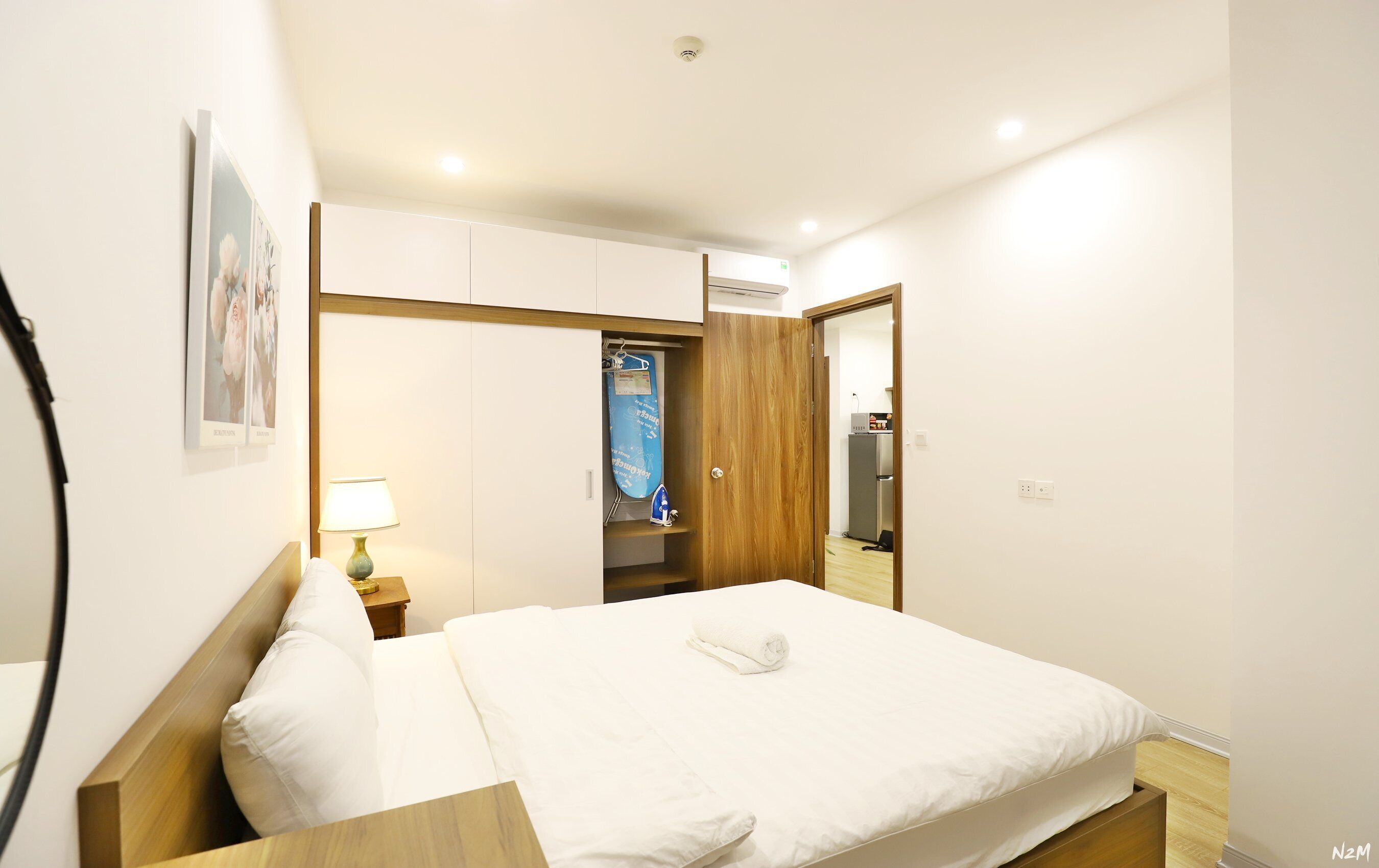 A hotel room with a bed, a nightstand, a lamp, a wardrobe, and an air conditioning unit.