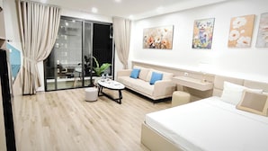 Una habitación de hotel moderna con un sofá, una mesa redonda de centro, una cama, un escritorio y una puerta corrediza de vidrio al balcón.