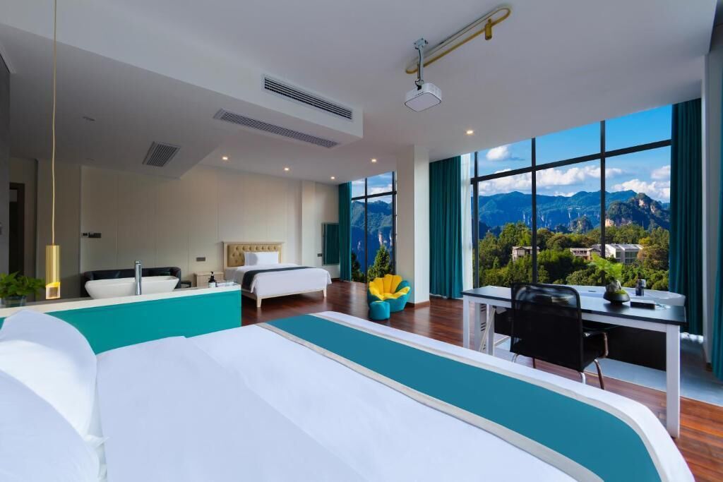 A modern hotel room with a large bed, a desk, and a view of mountains.