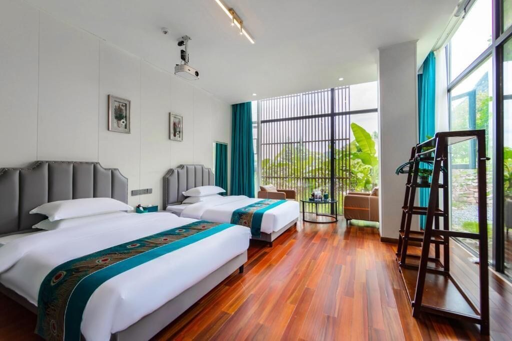 Habitación de hotel con dos camas, un ventanal grande y vistas a zonas verdes.