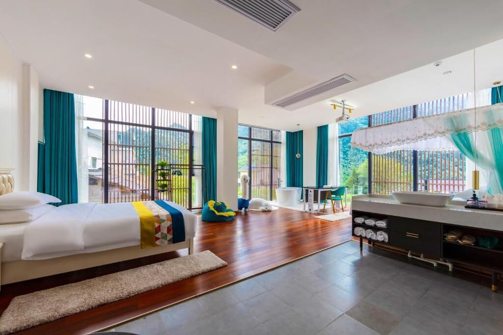 Une chambre d’hôtel moderne dotée d’un grand lit, d’un bureau, d’une chaise, d’une salle de bain avec un lavabo et de grandes fenêtres avec des rideaux.