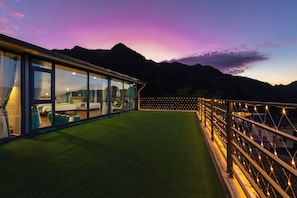 Un edificio moderno con amplios ventanales, un césped verde y montañas al fondo.