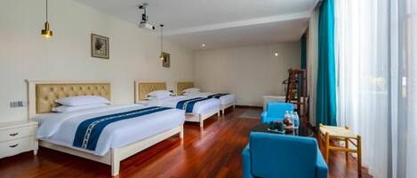 A hotel room with three beds, a blue armchair, a small table, and a large window with curtains.
