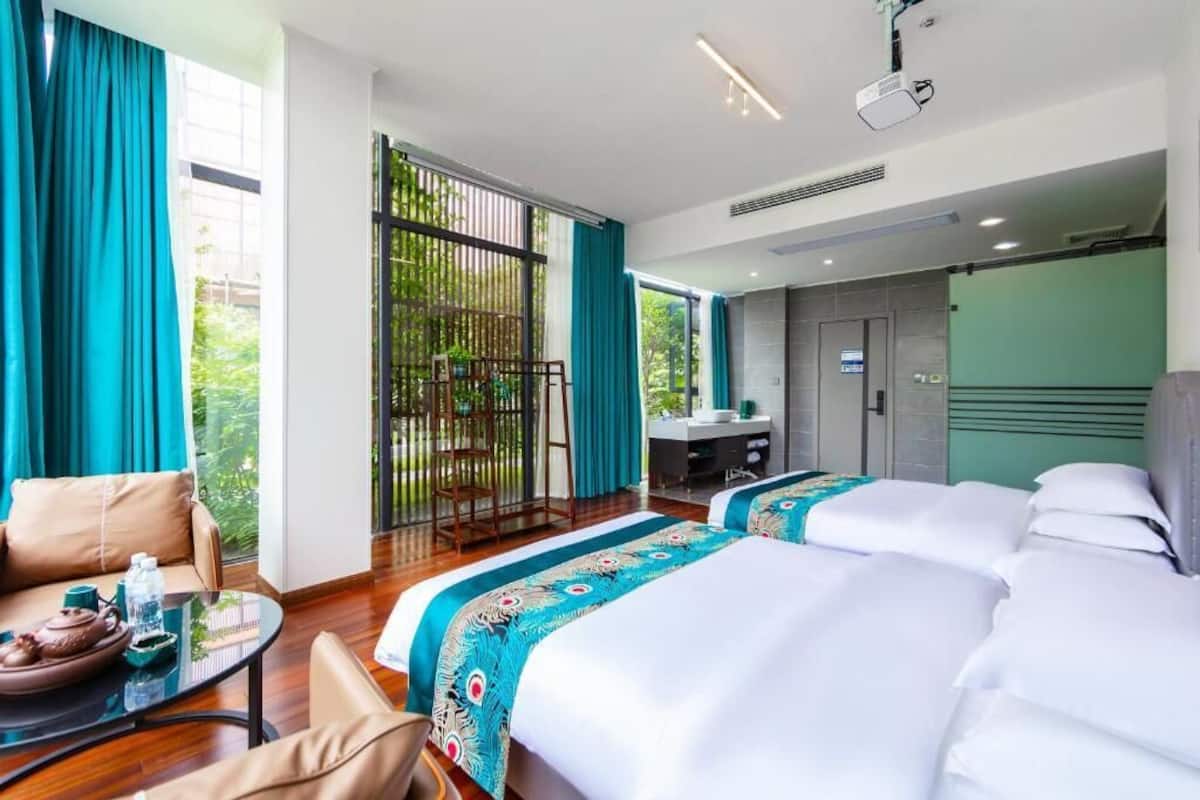 A hotel room with two beds, a sofa, a small table with a teapot, a desk, and a bathroom.