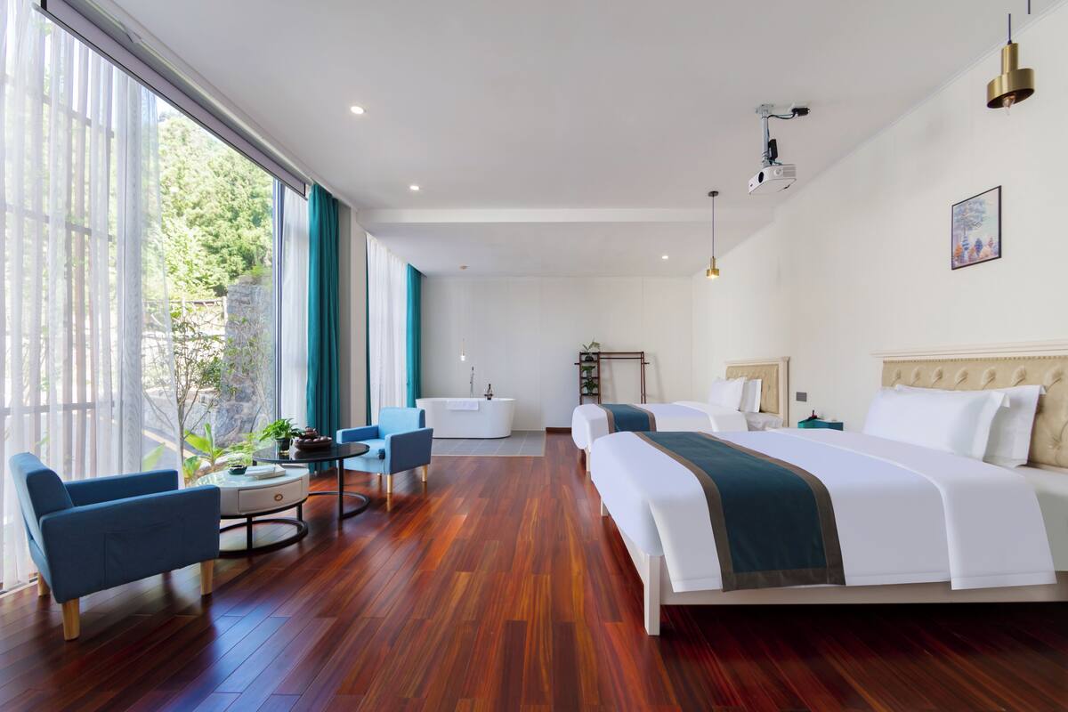 A modern hotel room with a large bed, a desk, a chair, and a view of the outdoors.