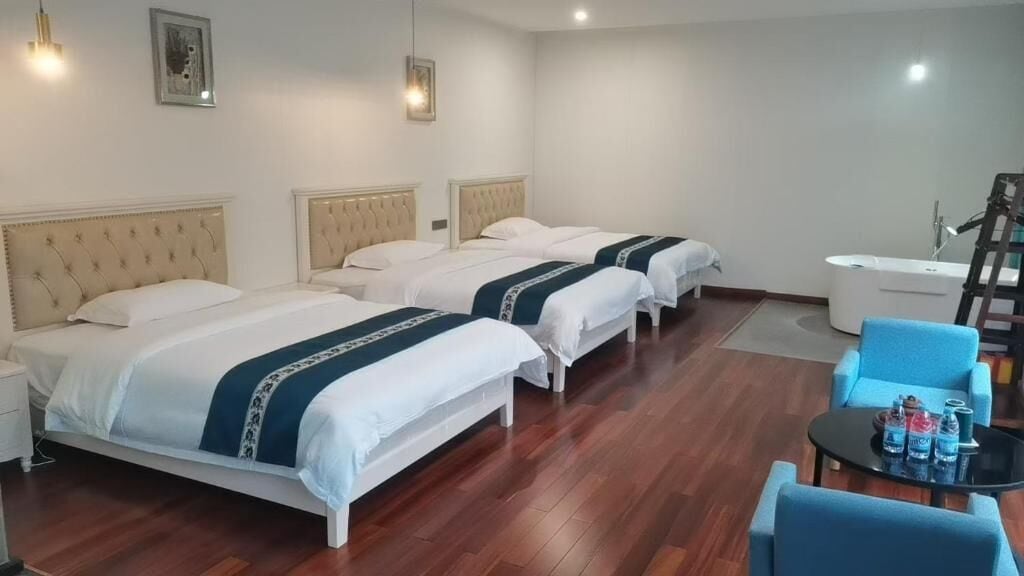 Ein Hotelzimmer mit drei Betten, einem kleinen Tisch mit Flaschen, einem Stuhl und einer Badewanne.