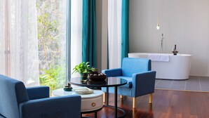 Une pièce moderne avec une table ronde, deux fauteuils bleus, un canapé blanc, une petite table blanche et une vue sur la verdure à l’extérieur.