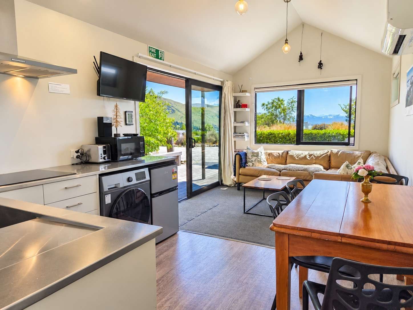 A modern kitchen with a dining area, a sofa, and a view of the outdoors.