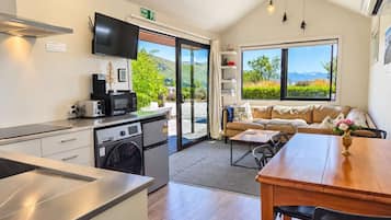 A modern kitchen with a dining area, a sofa, and a view of the outdoors.