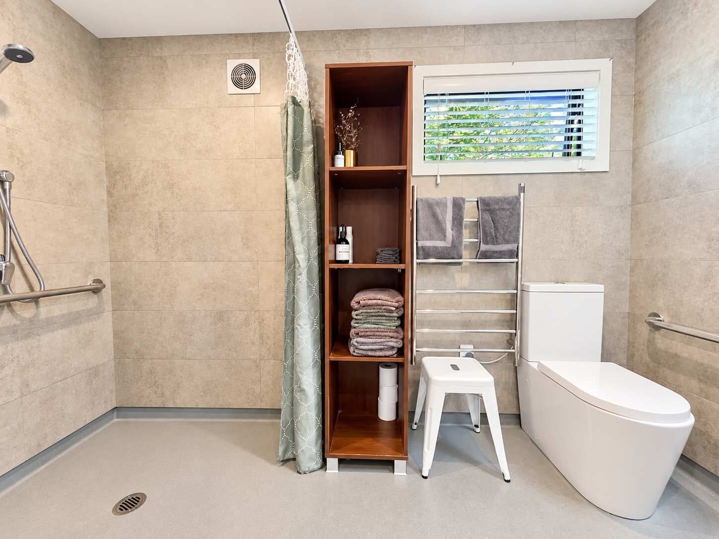 A bathroom with a shower, toilet, and a shelf with towels.