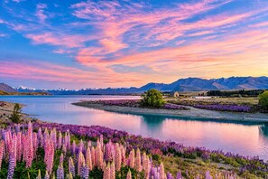 A landscape with a lake, mountains, and a small building. - Starfall | Lake Views + Cedar Tub | 2BR (Lake Tekapo)