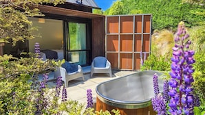 A modern outdoor seating area with a hot tub, a covered patio, and a view of a hillside. - The Black House Horizon Retreat -Private Outdoor Tub (Lake Tekapo)