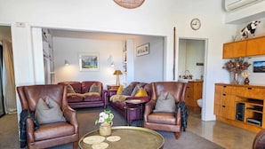 A living room with leather armchairs, a round coffee table, and a sofa. There is a painting on the wall, a lamp, and a clock. - The Black House Horizon Retreat -Private Outdoor Tub (Lake Tekapo)