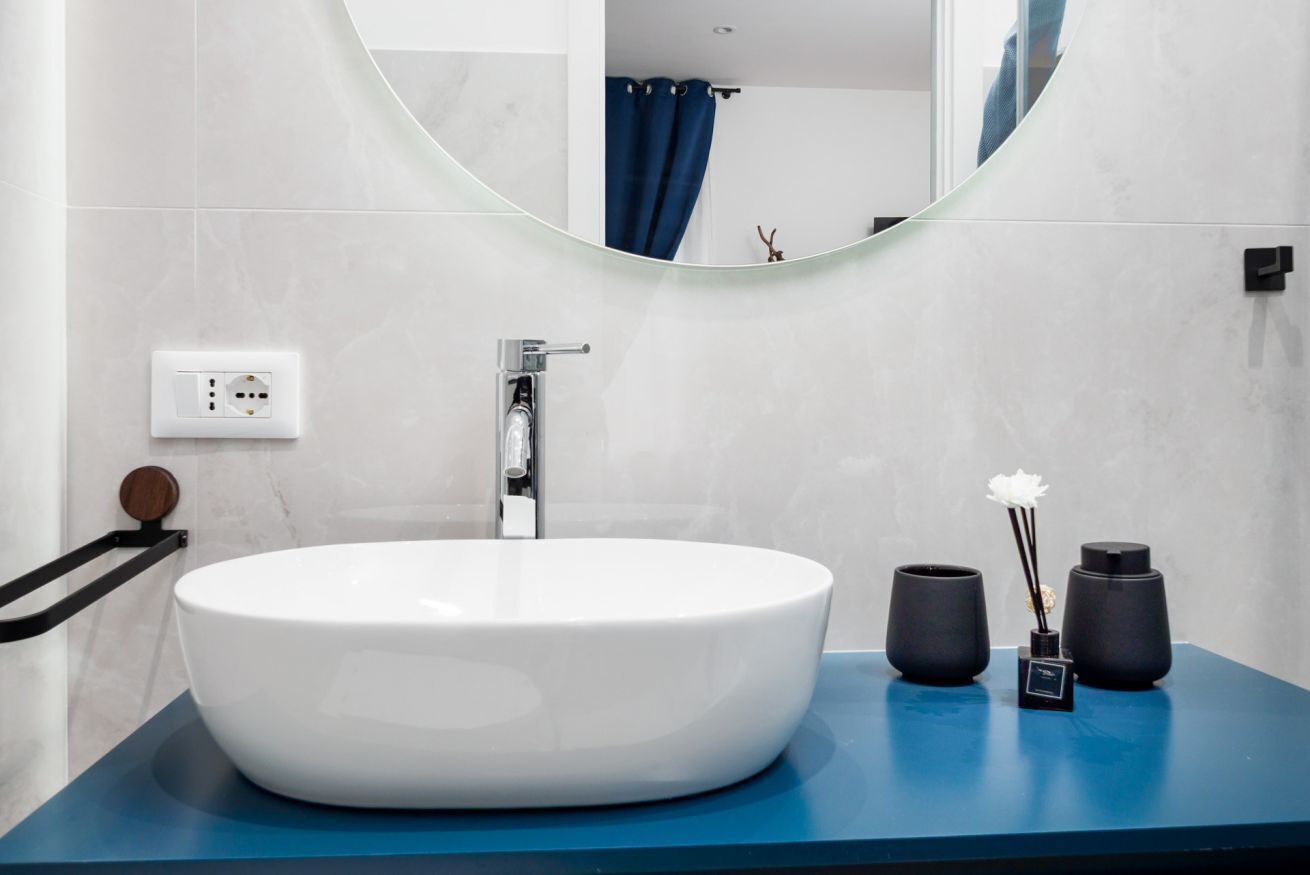 Une salle de bain moderne avec un grand lavabo ovale, un miroir rond et un plan de toilette bleu.