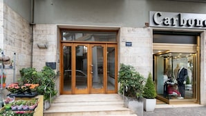 A storefront with a wooden entrance, potted plants, and a mannequin in the window.