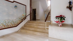 A staircase with a wooden handrail, a floral wall design, and a red potted plant.