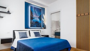 A modern bedroom with a large bed, a nightstand, a bedside table, a wall-mounted shelf, and a large painting above the bed.