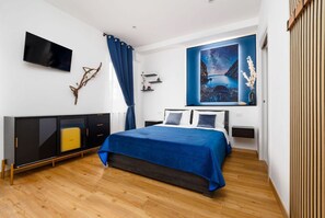 Una camera da letto moderna con un letto, una televisione, un quadro e un pavimento in legno.