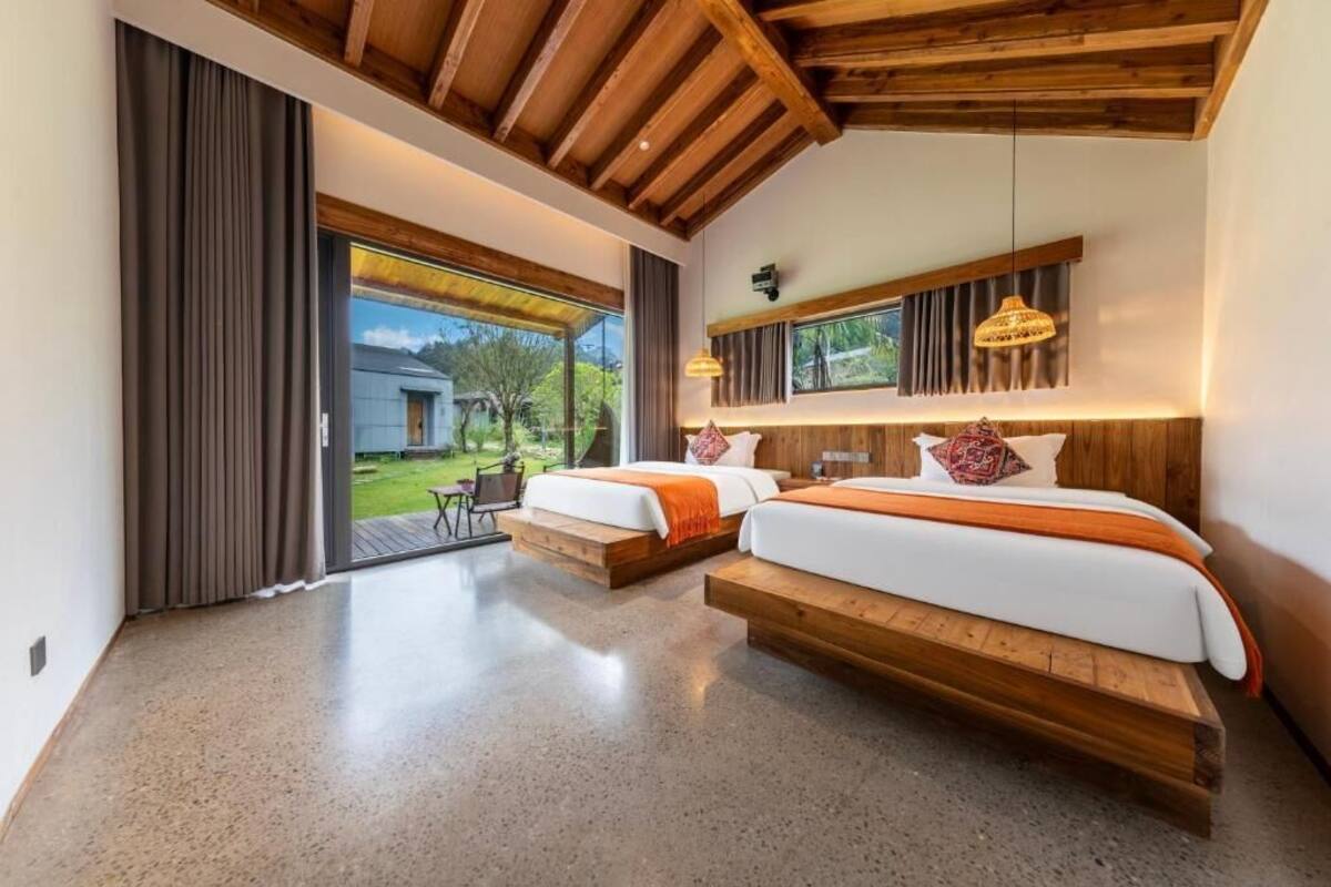 Un dormitorio moderno con dos camas, ventanas amplias y techo de madera.