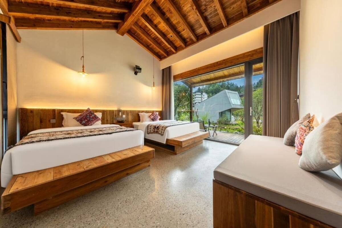 Un dormitorio con dos camas, vigas de madera, un ventanal grande y vistas a zonas verdes.