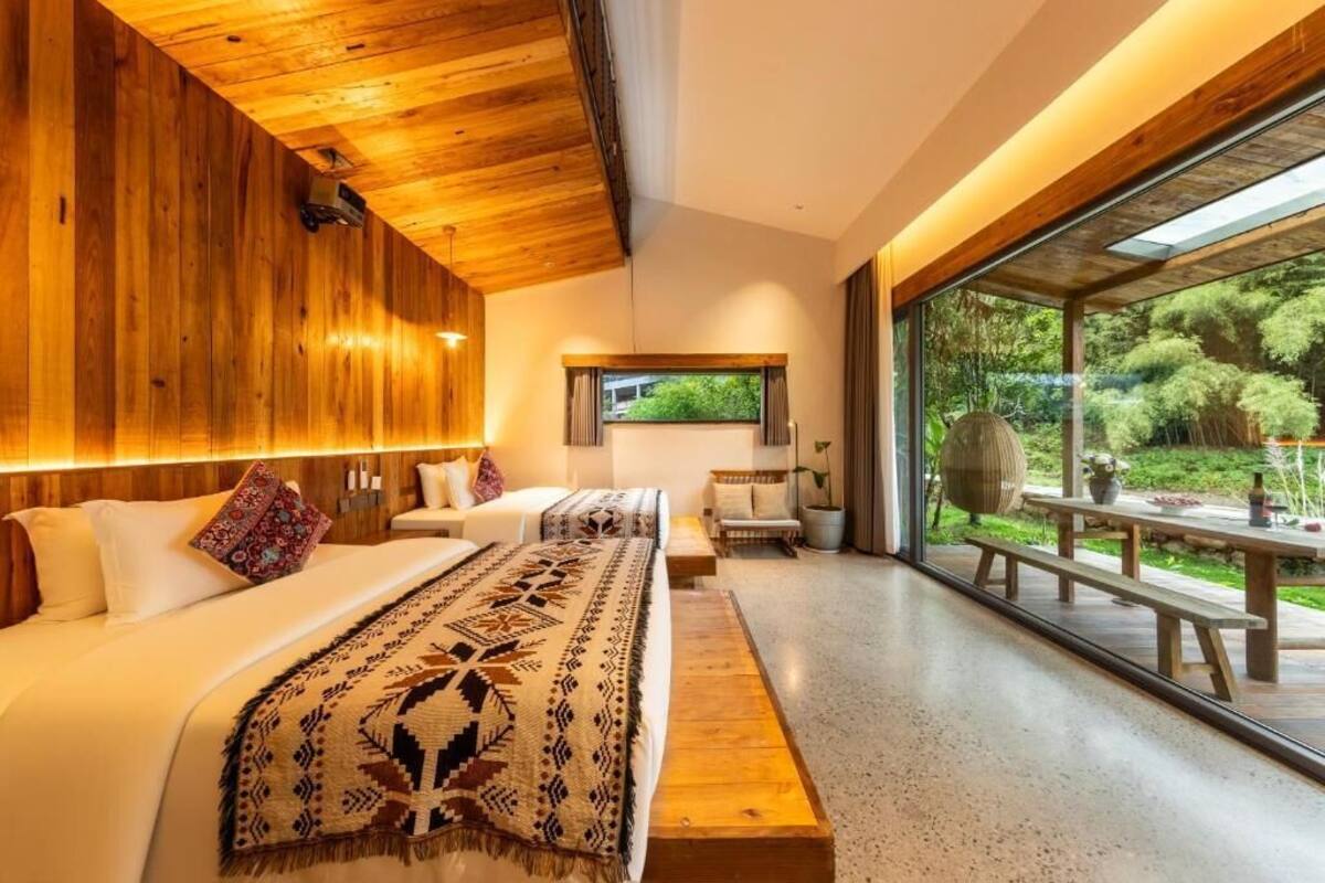 Una habitación de hotel moderna con un ventanal grande, techo de madera y una cama con una colcha estampada.