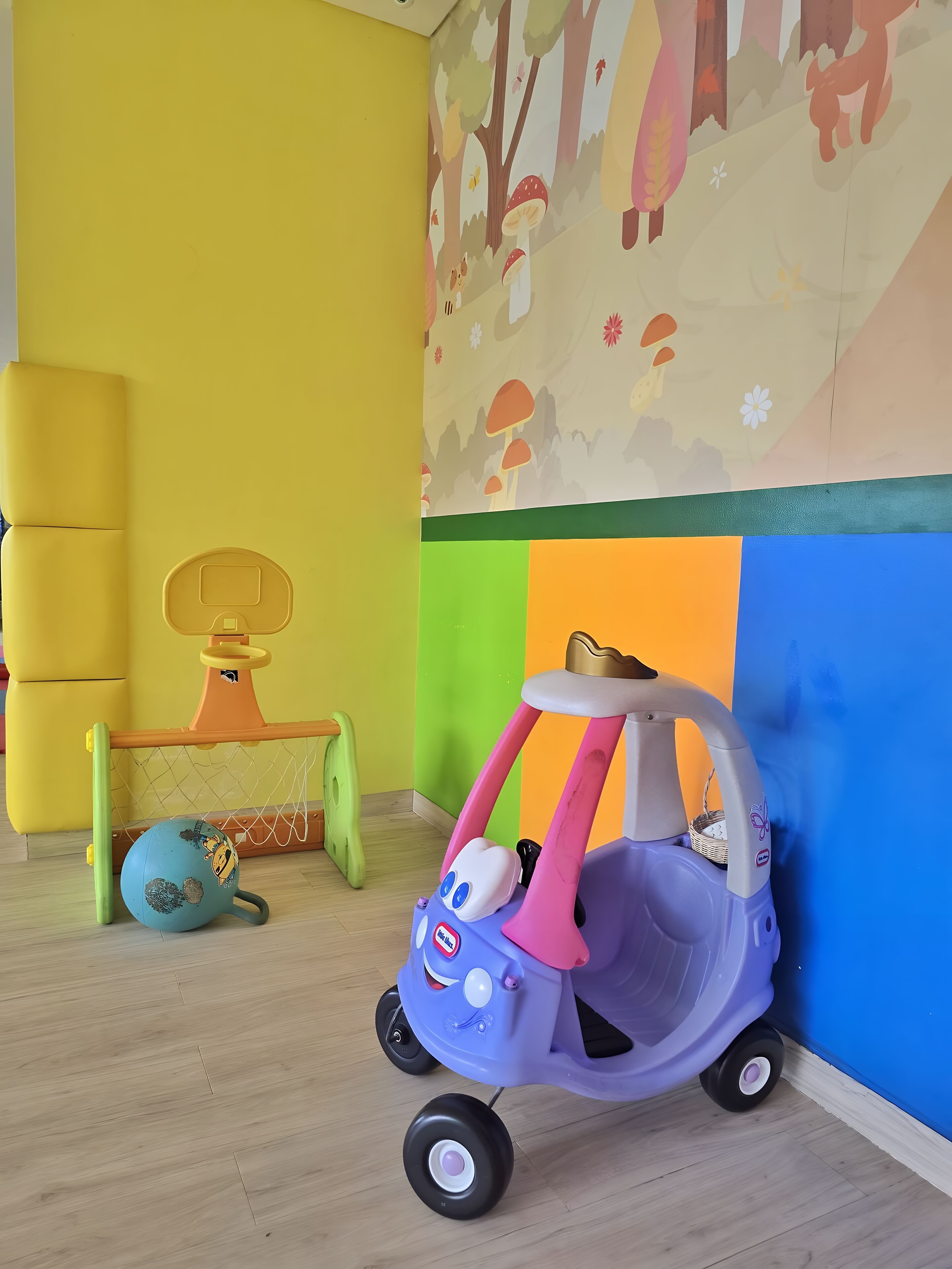 A child's toy car, a basketball hoop, and a globe on a wooden floor.