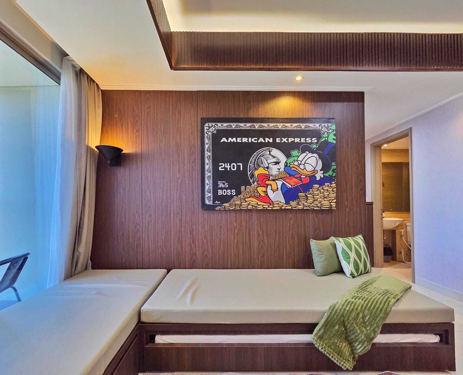 Une chambre d’hôtel avec un lit, une œuvre d’art représentant le logo d’American Express accrochée au mur, et une vue sur la salle de bain.