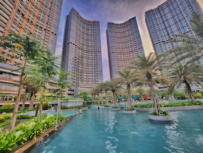 A modern residential building with high-rise apartments, a swimming pool, and palm trees. - By The Sky By SanLiving - 3BR - PIK (Jakarta)