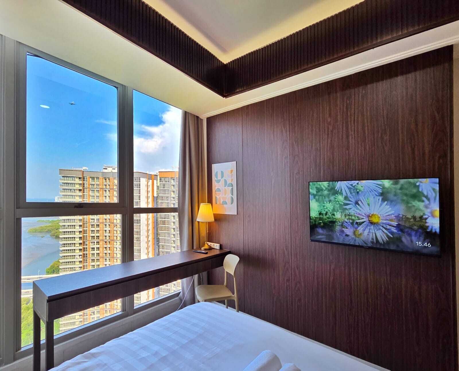 Ein Hotelzimmer mit großem Fenster, Schreibtisch, Stuhl, Bett und Wandfernseher.