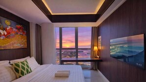 Une chambre d’hôtel avec un grand lit, une vue sur le paysage urbain au coucher du soleil, un tableau au mur et un téléviseur sur le côté.