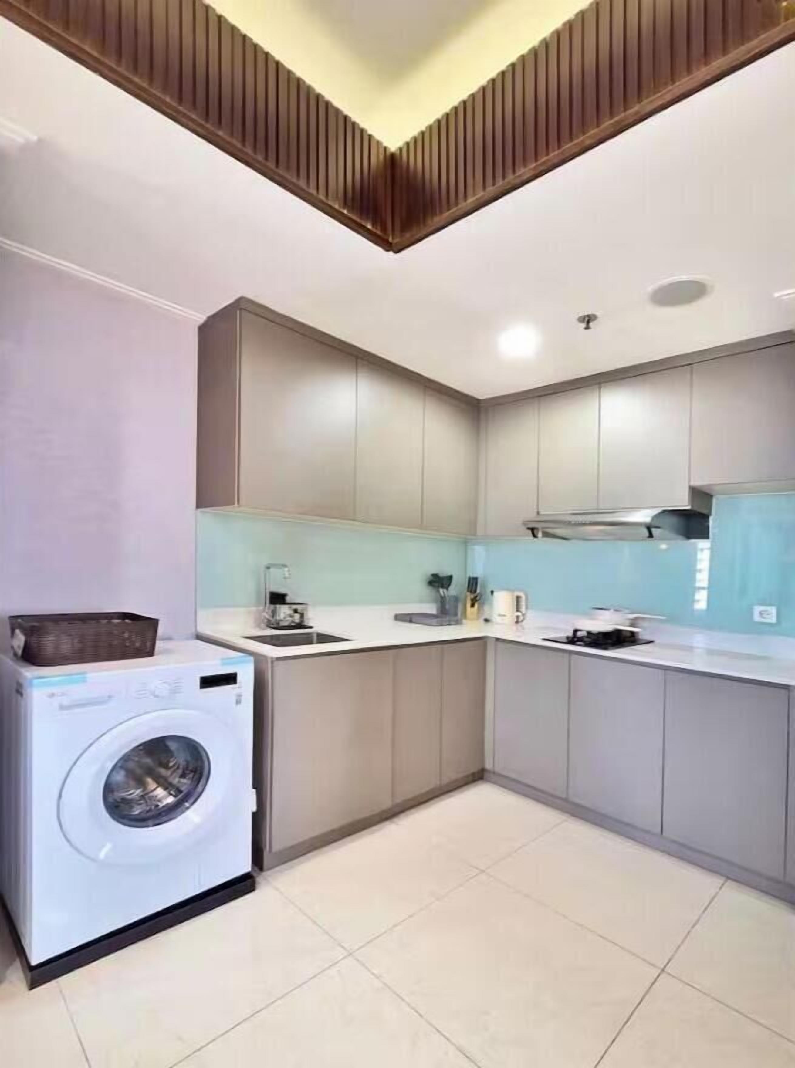 Een compacte keuken met een ingebouwde wasmachine, grijze kastjes en een modern plafond.