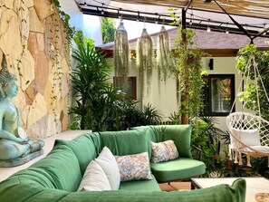 A green sofa with cushions, a hanging chair, and a Buddha statue in a garden setting with plants and hanging lights. - Azure Garden Villa, close to ChoengMon beach (Koh Samui)